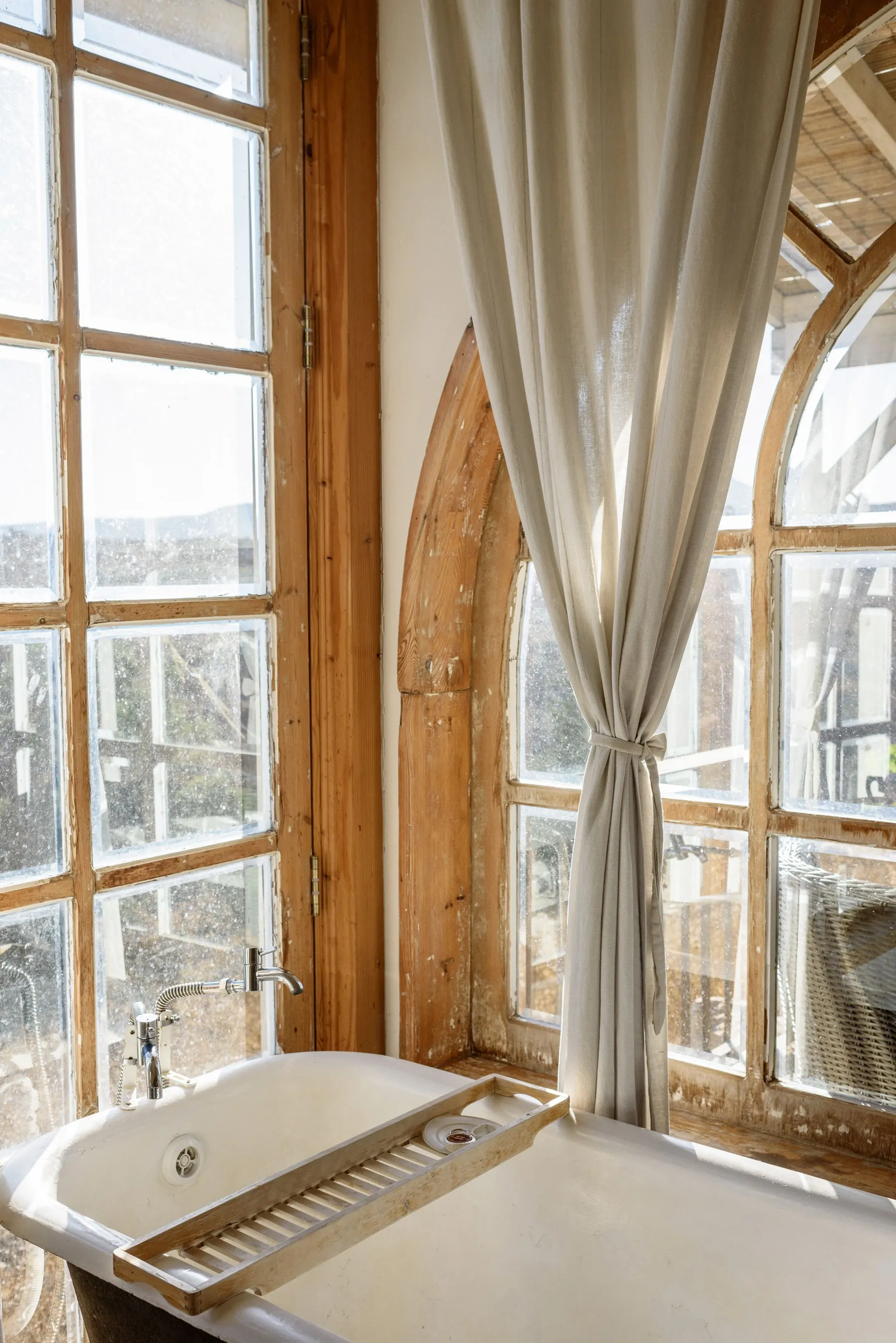 Bright bathroom with a bath under tall wooden windows